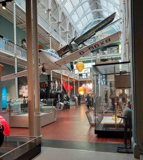 A hot-air balloon ascending among aircraft above the Wylam Dilly locomotive in the National Museum of Scotland.