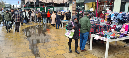 A busy street corner with traders tables occupying part of the pavement.